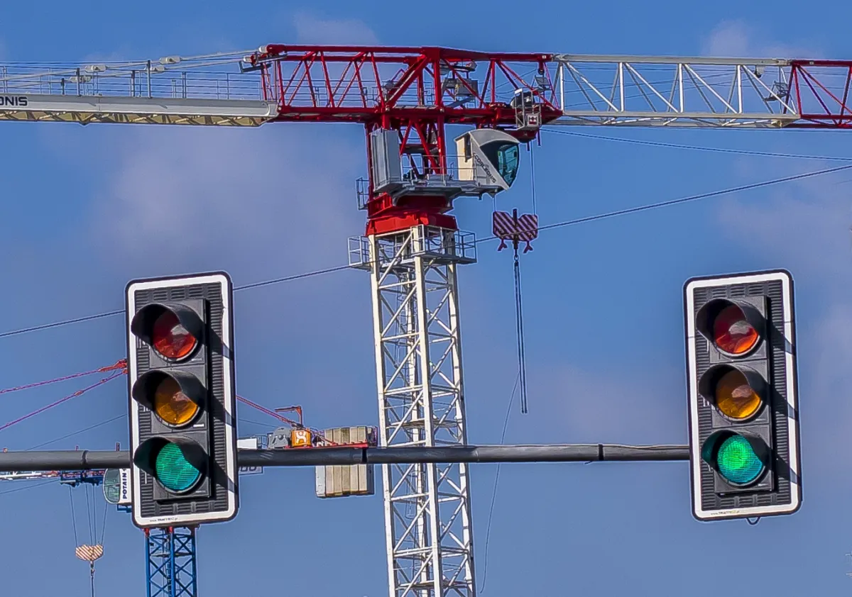 Traffic lights hanging in front of a red-and-white construction crane